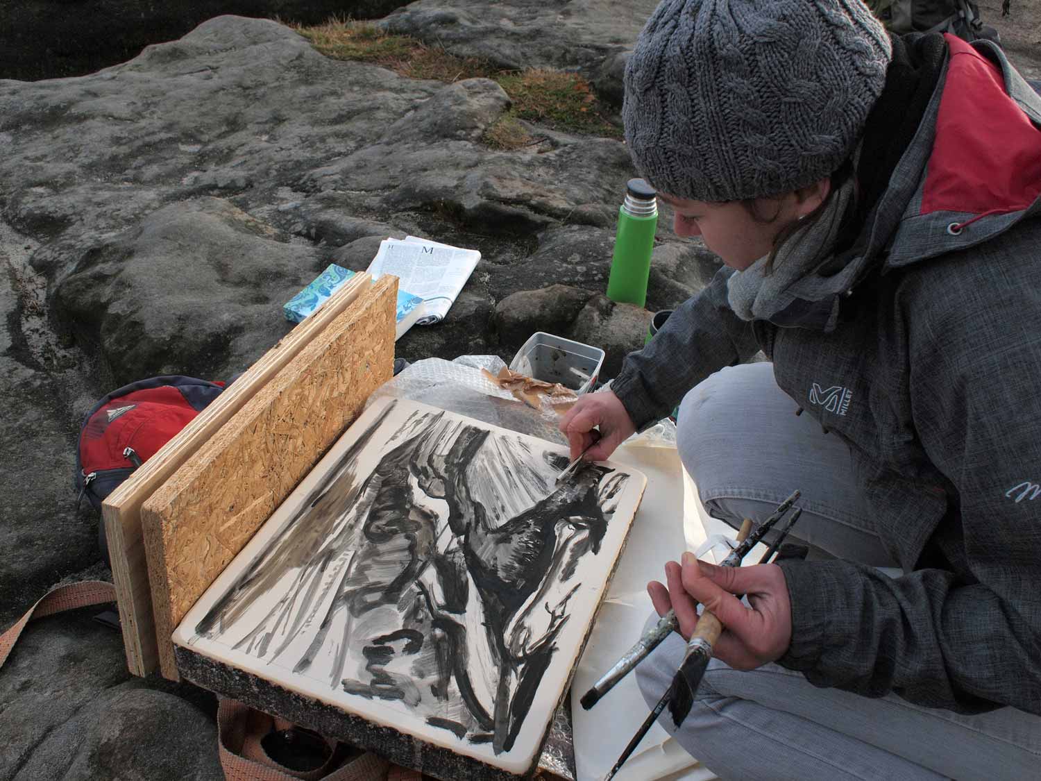 Künstlerin Yvette Kießling bei der Bearbeitung eines Lithographie-Steines mit Pinseln in der linken Hand auf felsigem Untergrund.